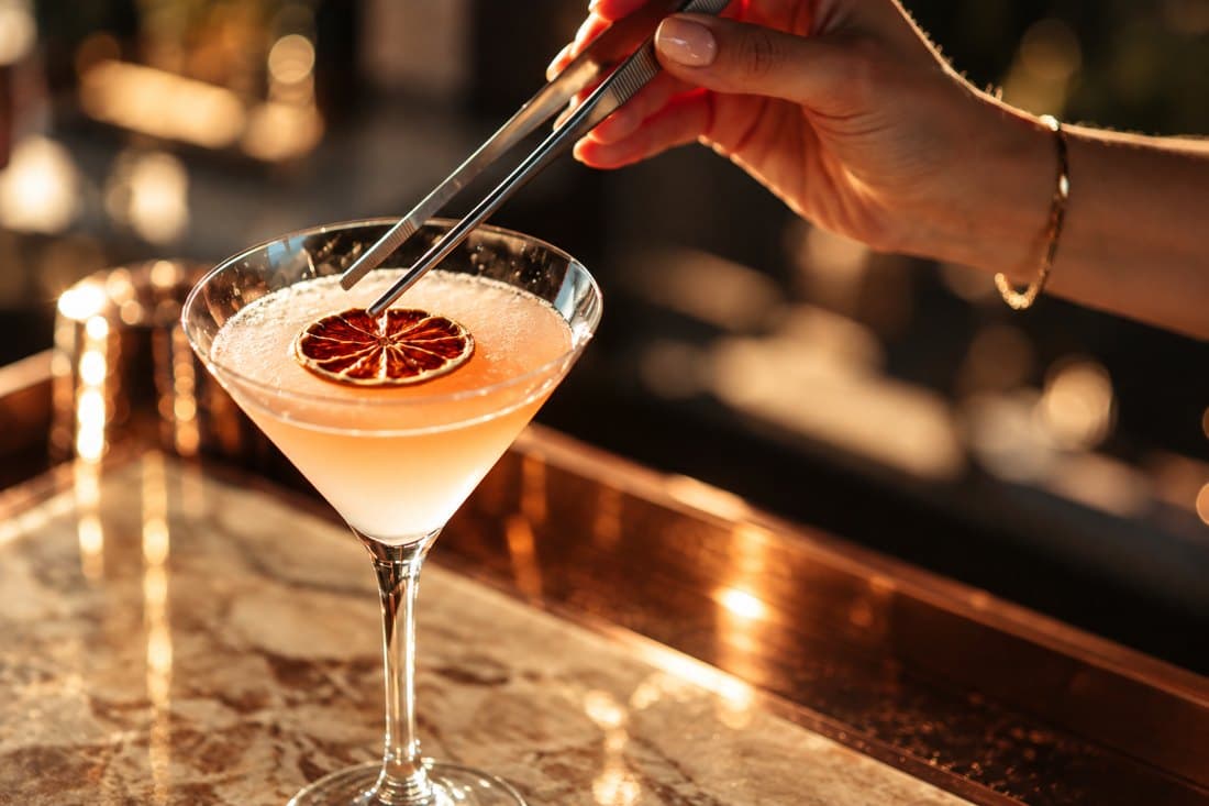 Garnitura unui cocktail roz, așezată cu penseta, pe blat de cupru
